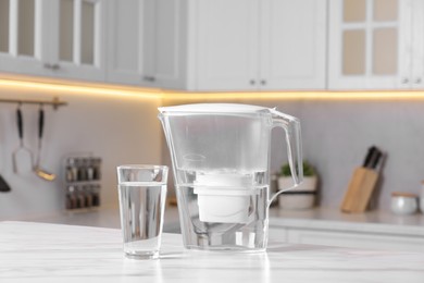 Photo of Water filter jug and glass on white marble table in kitchen, closeup