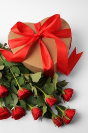 Photo of Heart shaped gift box with bow and beautiful red roses on white background, above view