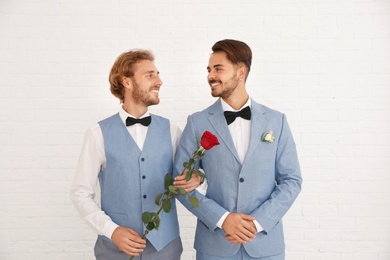 Photo of Happy newlywed gay couple with flower against white wall