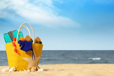 Photo of Bag with beach objects on sand near sea, space for text