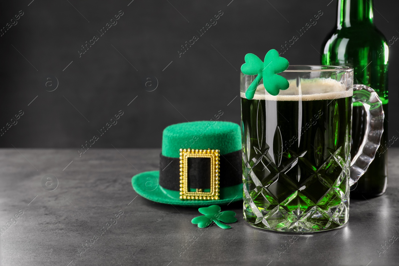 Photo of St. Patrick's day celebration. Green beer, leprechaun hat and decorative clover leaves on grey table. Space for text