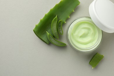 Photo of Jar with cream and cut aloe leaf on light grey background, flat lay. Space for text