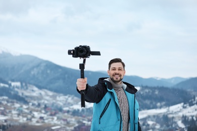 Photo of Man with stabilizer and camera recording video in mountains. Winter vacation