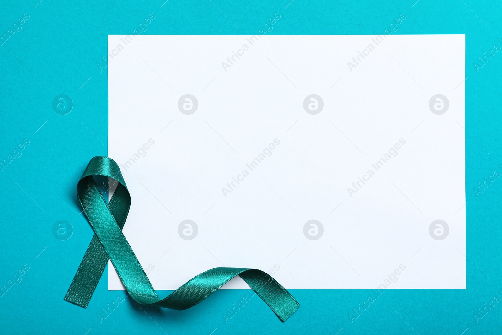 Photo of Teal ribbon and blank card on color background, top view. Space for text