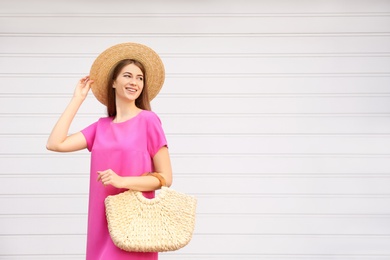 Photo of Beautiful young woman with stylish straw bag near white wall. Space for text