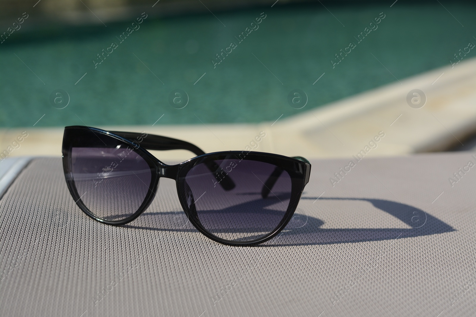 Photo of Stylish sunglasses near outdoor swimming pool on sunny day, space for text