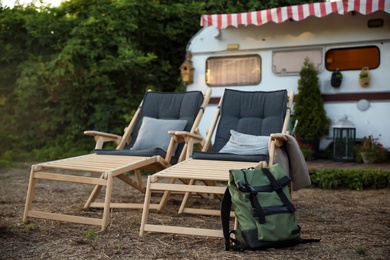 Photo of Deck chairs and backpack near modern trailer. Camping season
