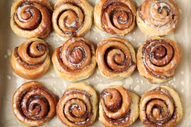 Tasty cinnamon rolls with cream on parchment paper, flat lay