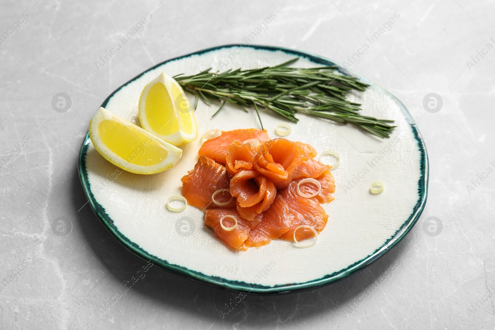 Photo of Plate with fresh sliced salmon fillet, lemon and rosemary on table