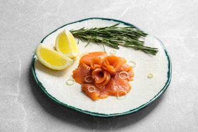 Photo of Plate with fresh sliced salmon fillet, lemon and rosemary on table