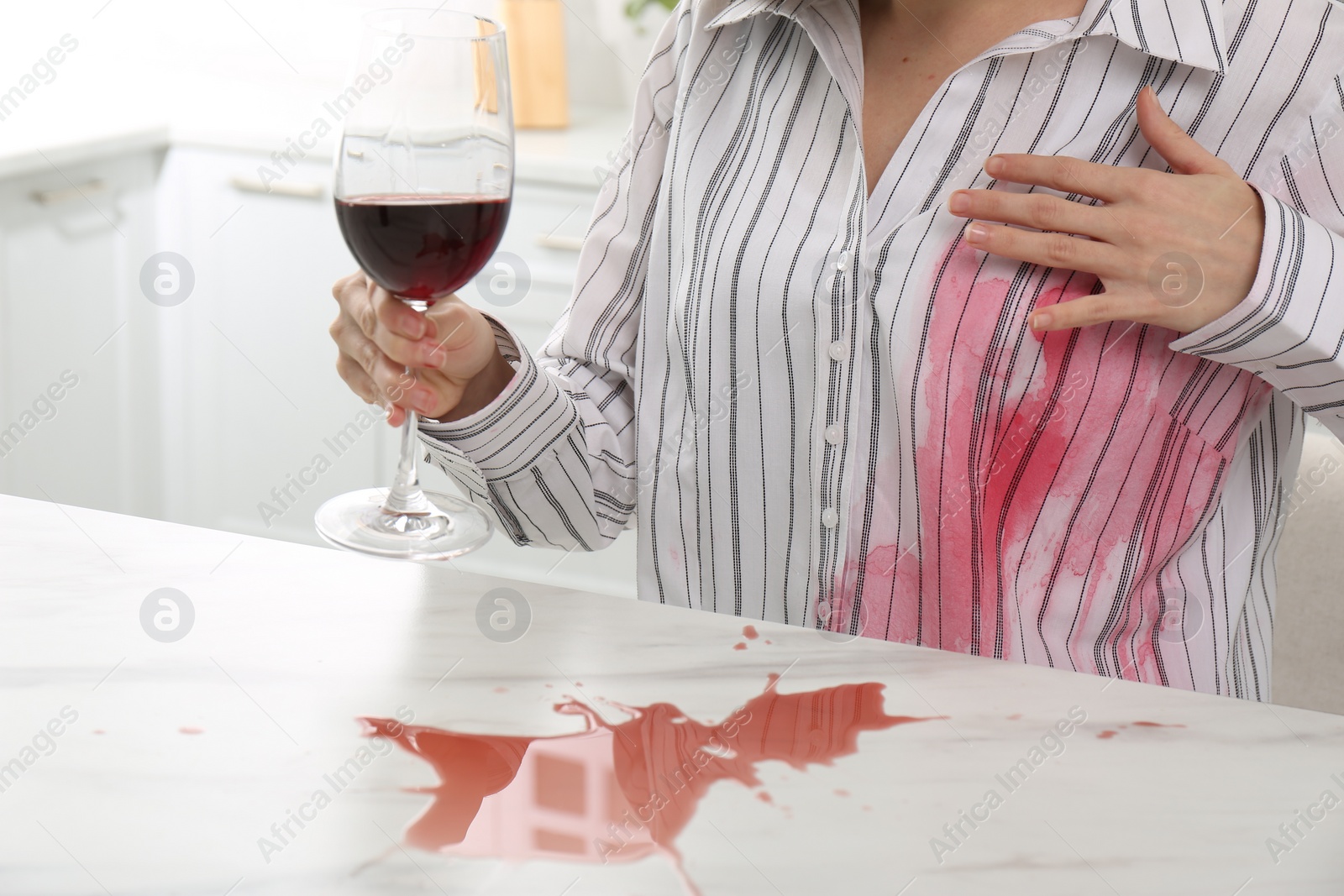 Photo of Woman with spilled wine over her shirt and marble table in kitchen, closeup