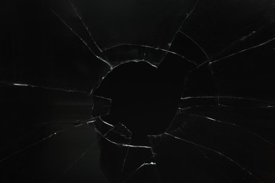 Photo of Closeup view of broken glass with cracks on black background