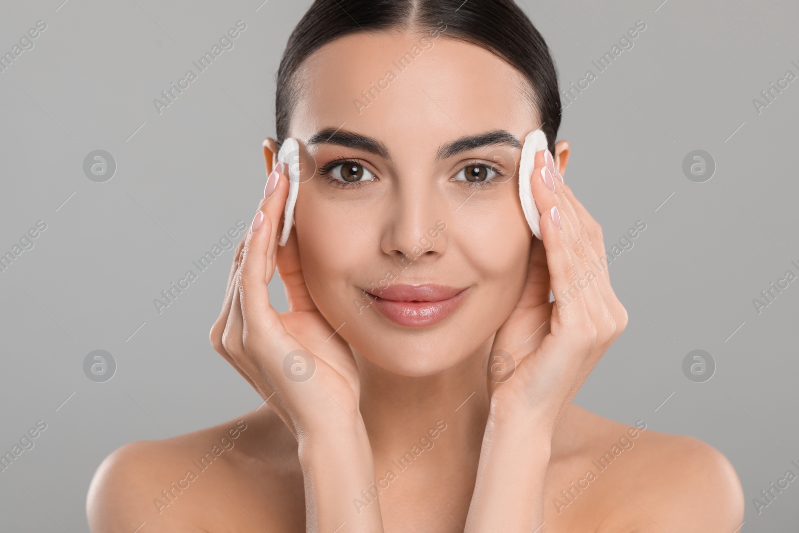 Photo of Beautiful woman removing makeup with cotton pads on light grey background