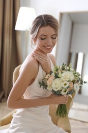 Beautiful young bride in elegant wedding dress with bouquet sitting in armchair