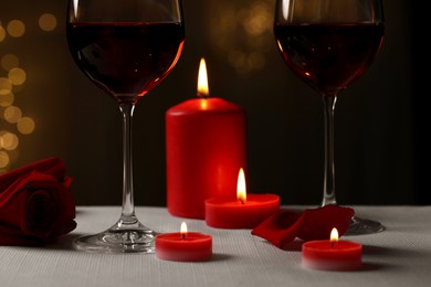 Photo of Glasses of red wine, burning candles and rose flower on grey table against blurred lights. Romantic atmosphere