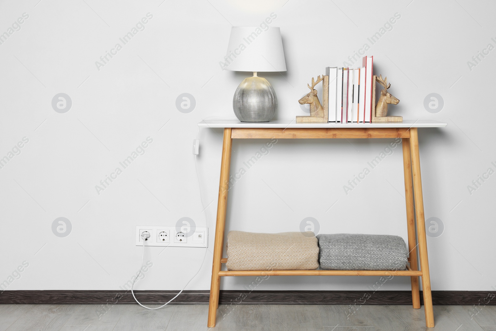 Photo of Lamp with books on wooden table near white wall, space for text