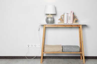 Photo of Lamp with books on wooden table near white wall, space for text