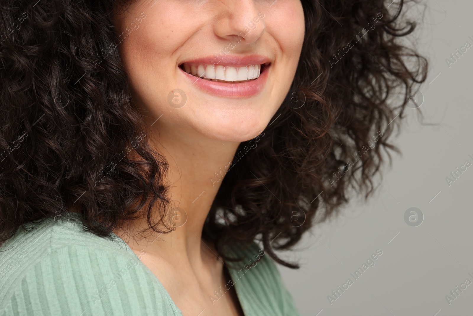 Photo of Young woman using teeth whitening strip on grey background, closeup. Space for text