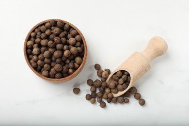 Photo of Dry allspice berries (Jamaica pepper) in bowl and scoop on white marble table, flat lay