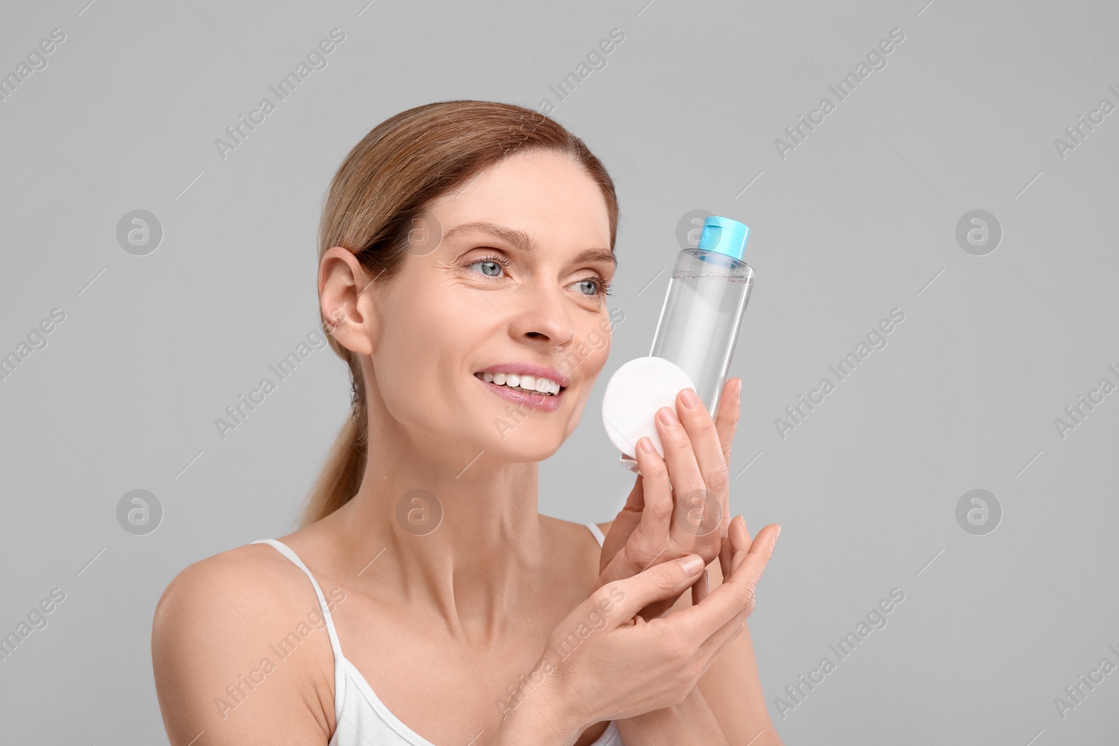 Photo of Beautiful woman with makeup remover and cotton pad on gray background