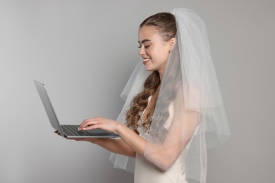 Photo of Happy bride with laptop on gray background