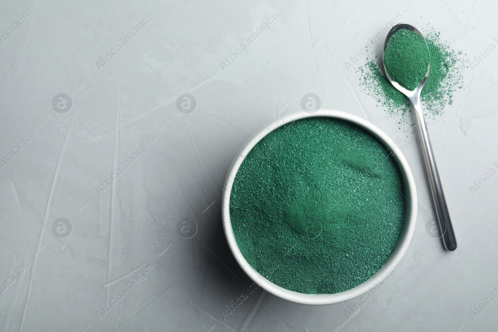 Photo of Bowl and spoon of spirulina algae powder on grey background, top view with space for text