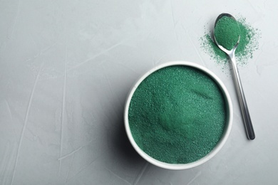 Photo of Bowl and spoon of spirulina algae powder on grey background, top view with space for text