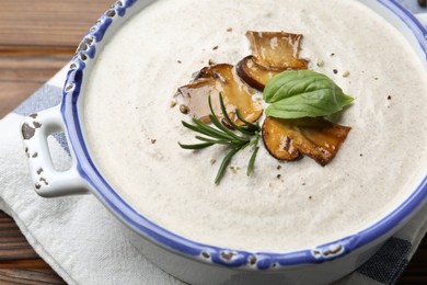 Delicious homemade mushroom soup in ceramic pot and fresh ingredients on wooden table, closeup