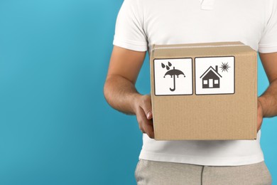 Photo of Courier holding cardboard box on light blue background, closeup. Space for text