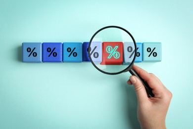 Image of Best mortgage interest rate. Woman looking at red cube with percent sign through magnifying glass on cyan background, top view