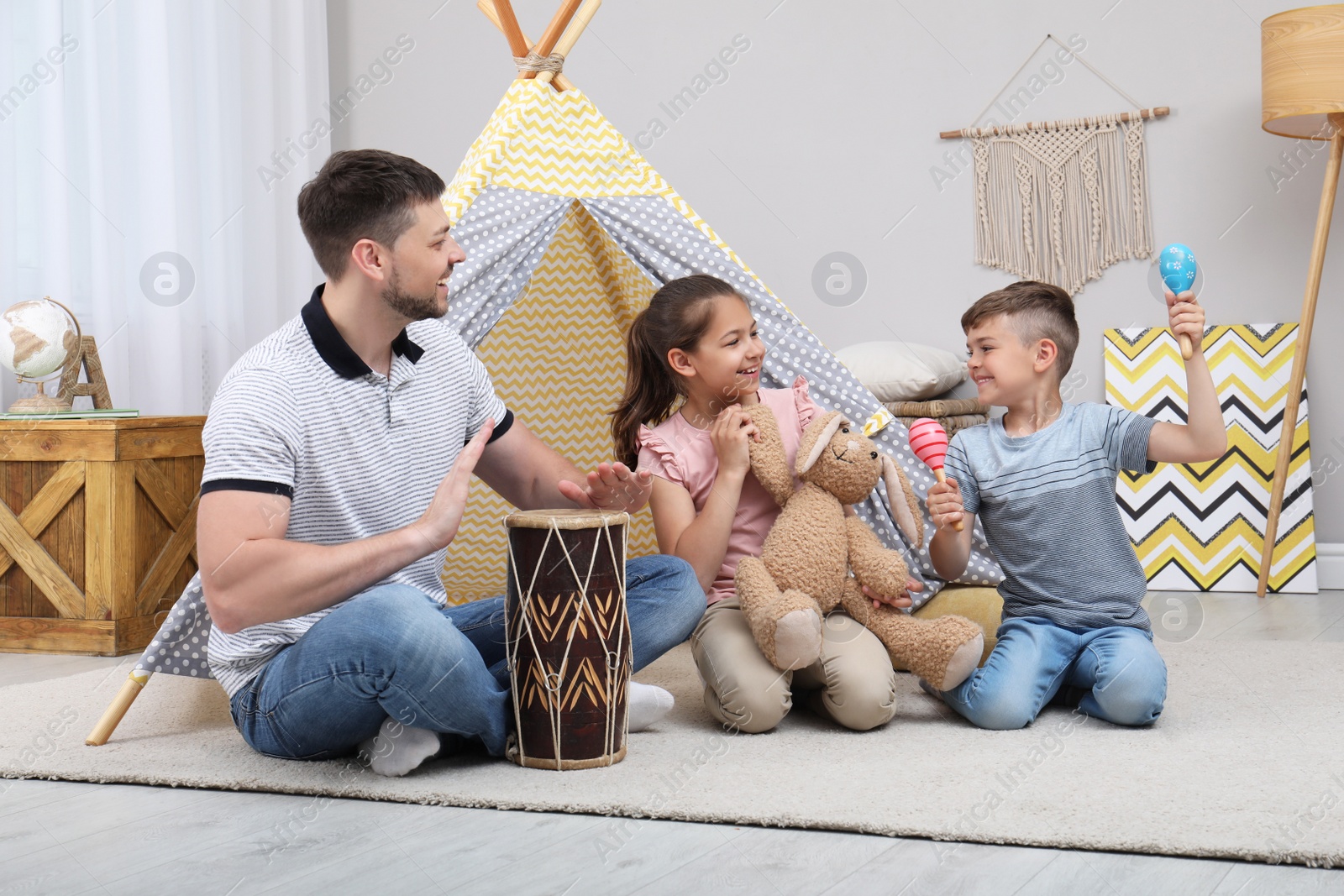 Photo of Father and children playing near toy wigwam at home