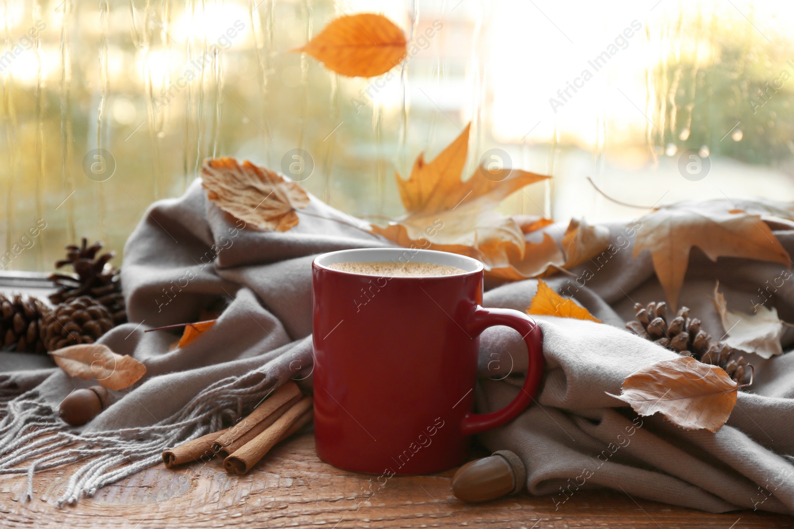 Photo of Cup of hot drink, scarf and autumn leaves on windowsill. Cozy atmosphere