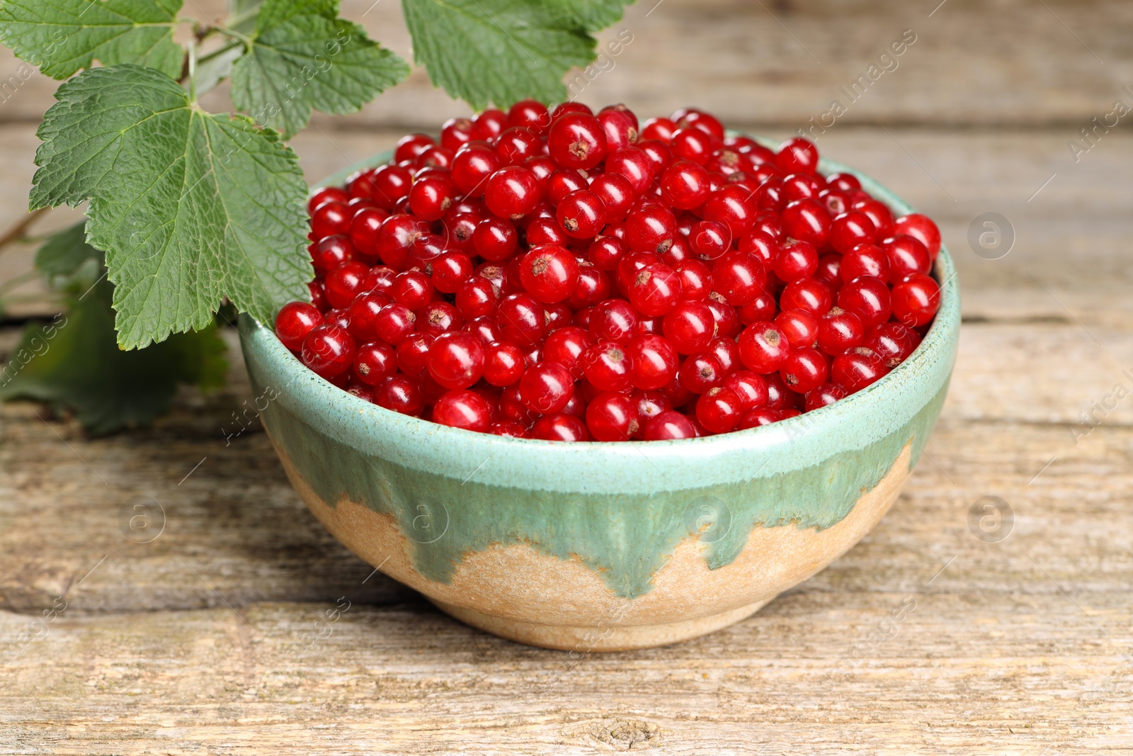 Photo of Ripe red currants in bowl on wooden table, closeup