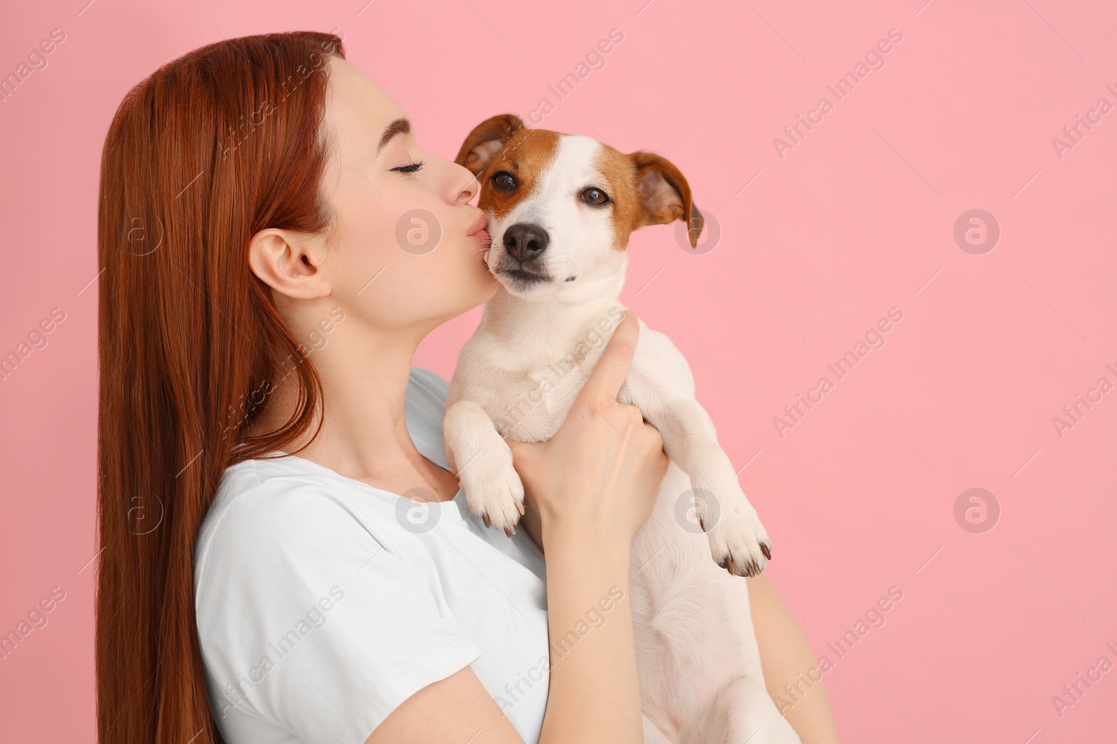 Photo of Woman kissing her cute Jack Russell Terrier dog on pink background. Space for text