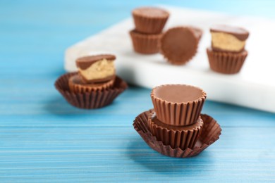 Photo of Delicious peanut butter cups on light blue wooden table, space for text
