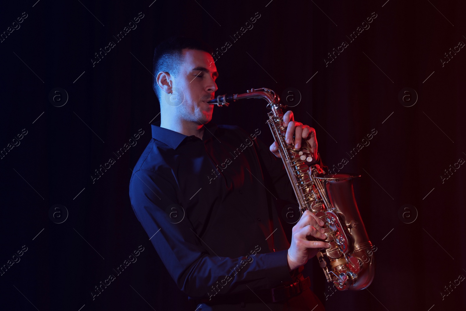 Photo of Young man playing saxophone on dark background