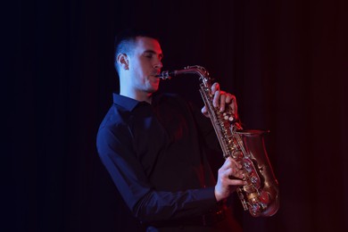 Photo of Young man playing saxophone on dark background