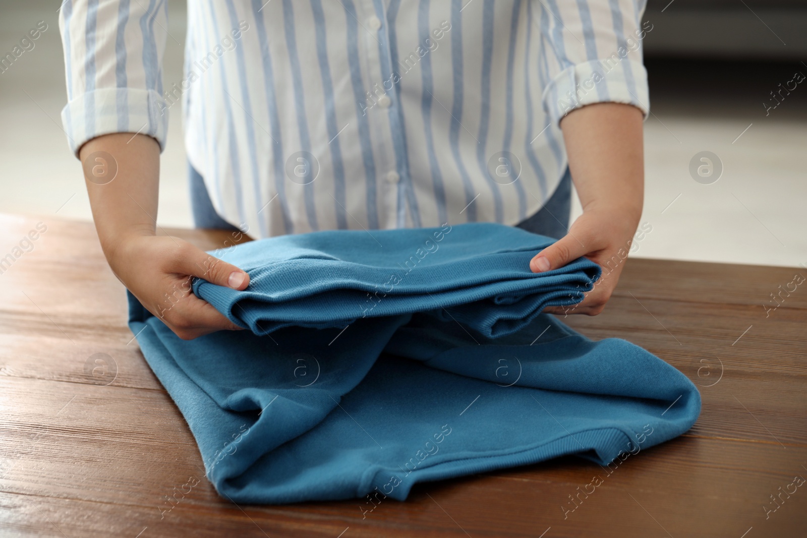 Photo of Woman folding clothes at wooden table indoors, closeup