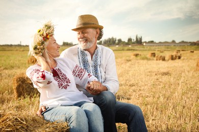Photo of Happy mature couple wearing Ukrainian national clothes on hay bale in field