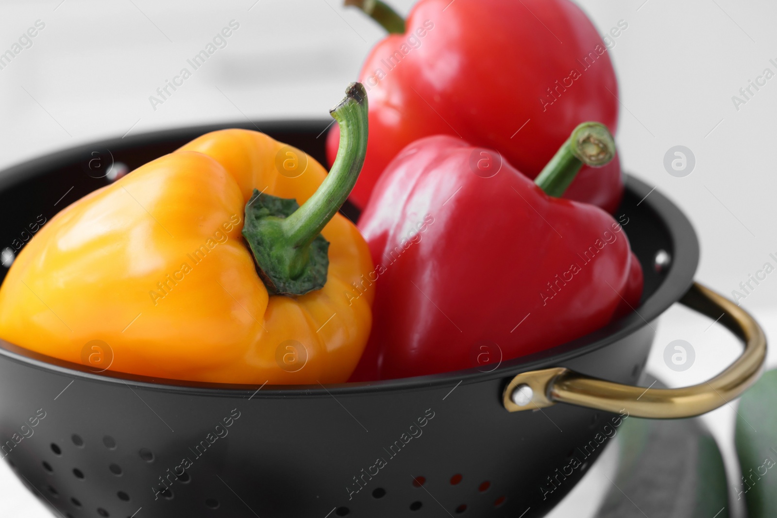 Photo of Fresh bell peppers in black colander on blurred background, closeup