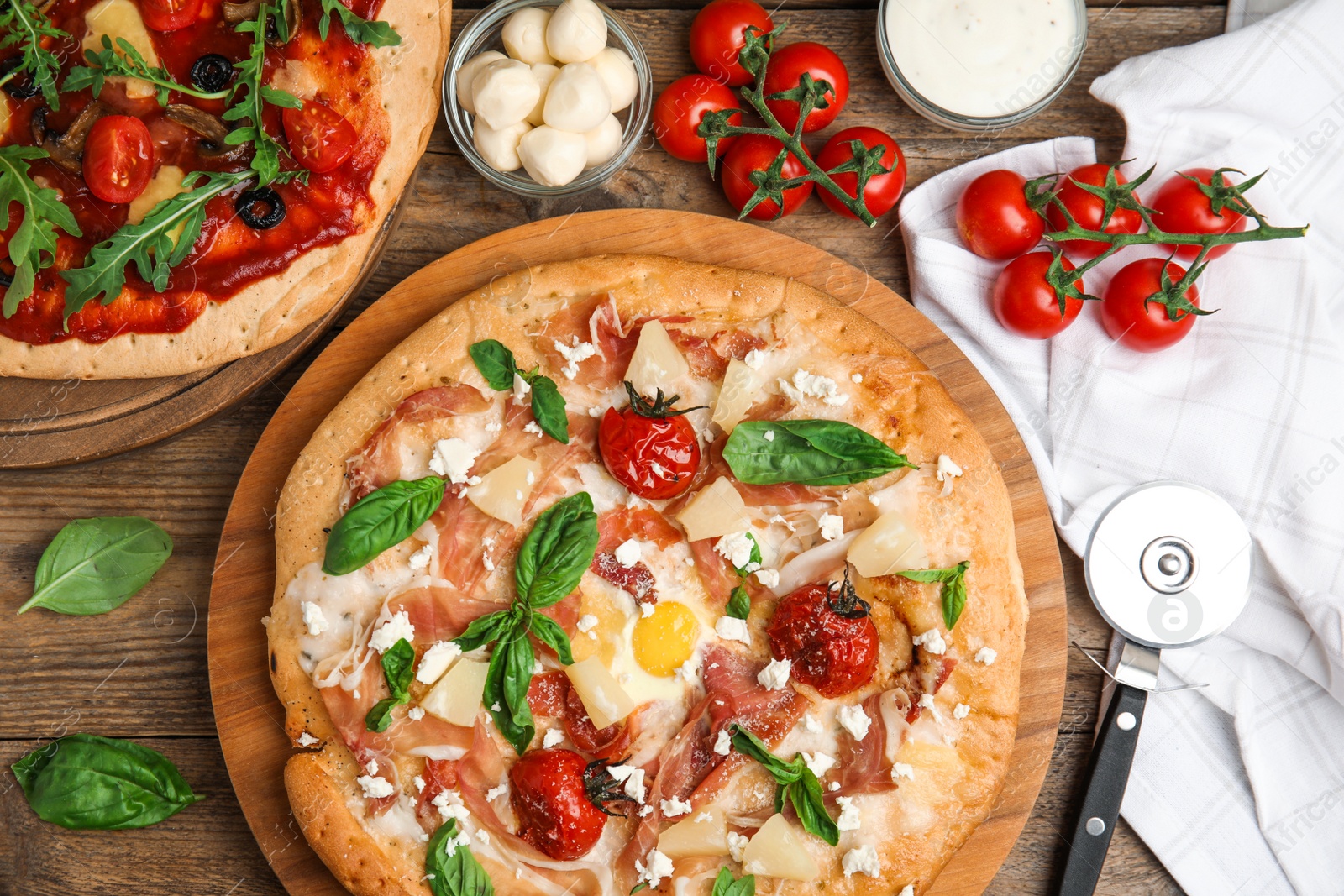 Photo of Delicious pita pizzas with prosciutto, pineapple, grilled tomatoes and egg on wooden table, flat lay