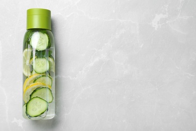 Photo of Bottle of refreshing water with cucumber, lemon and mint on light grey table, top view. Space for text