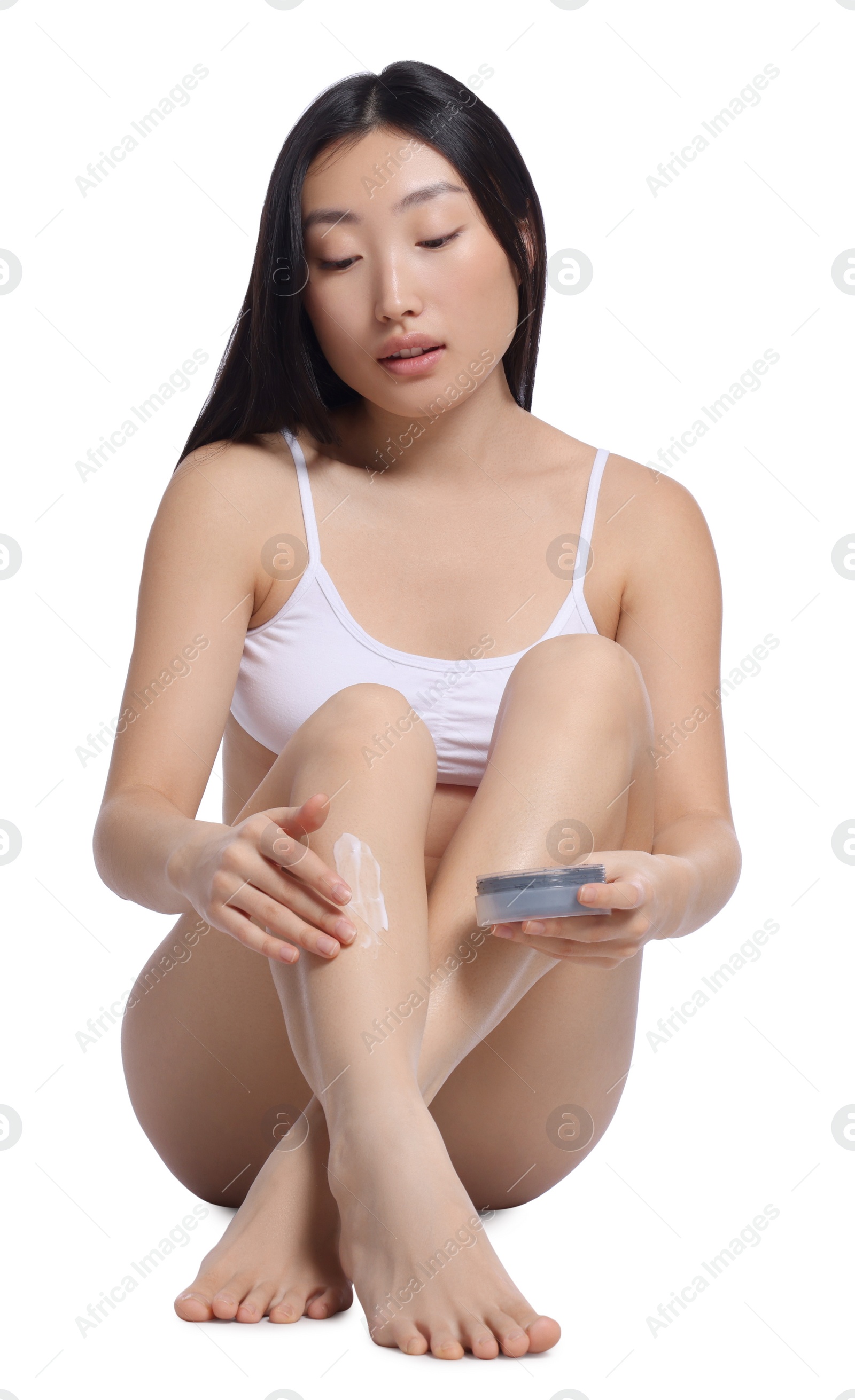 Photo of Beautiful young Asian woman applying body cream onto legs on white background