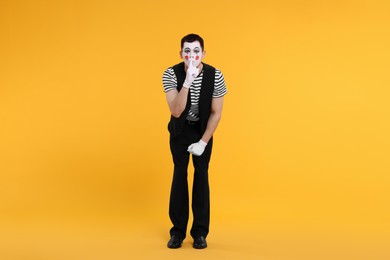 Photo of Funny mime artist showing hush gesture on orange background
