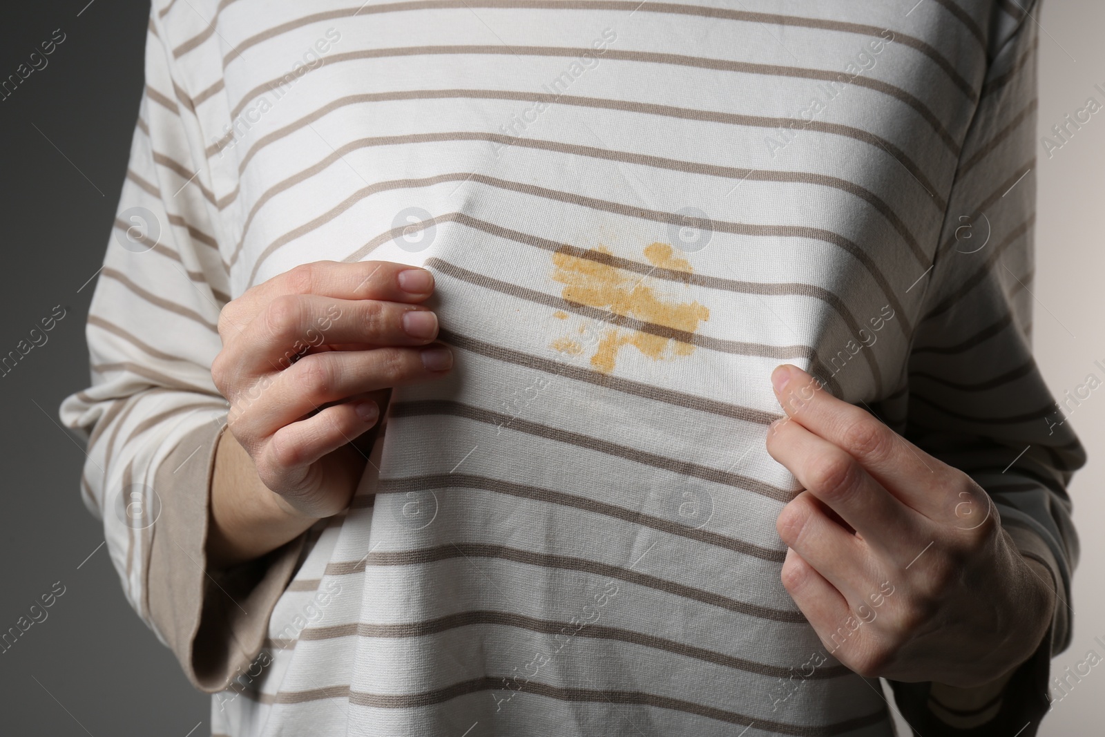 Photo of Woman showing shirt with yellow stain on grey background, closeup