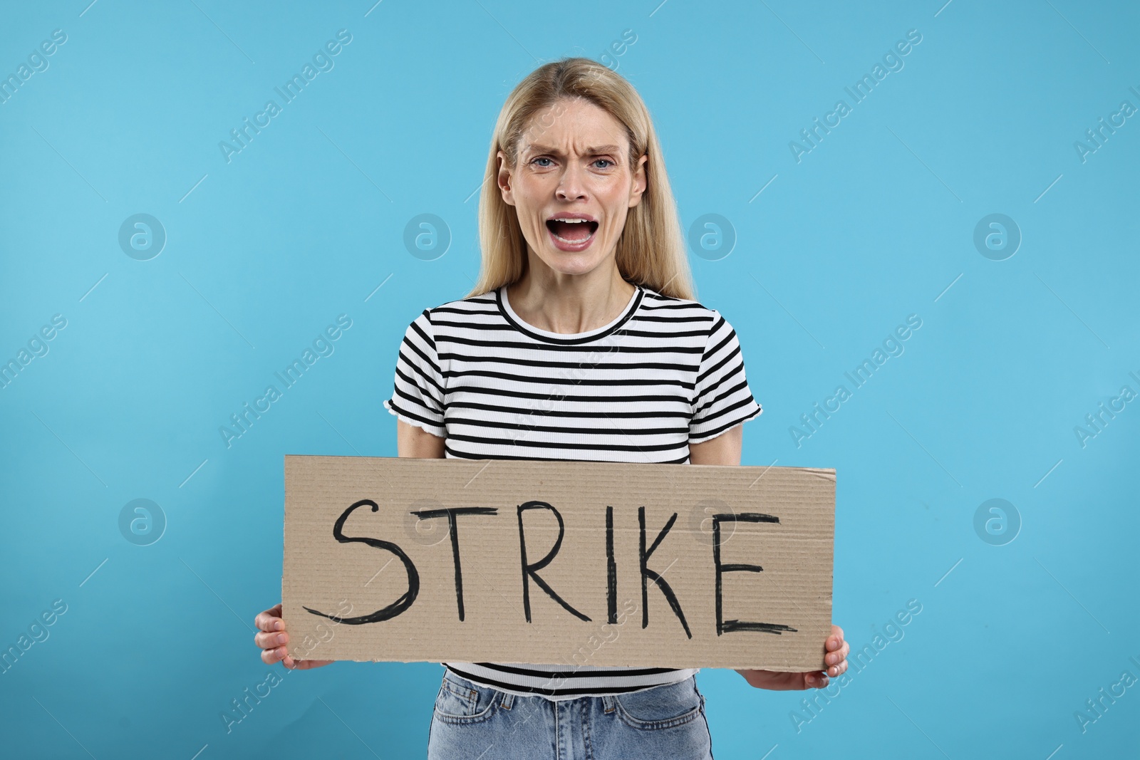 Photo of Angry woman holding cardboard banner with word Strike on light blue background