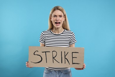 Photo of Angry woman holding cardboard banner with word Strike on light blue background