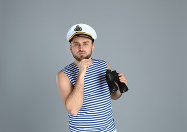 Thoughtful sailor with binoculars on light grey background