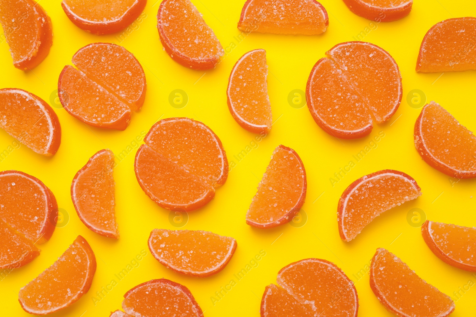 Photo of Delicious orange marmalade candies on yellow background, flat lay