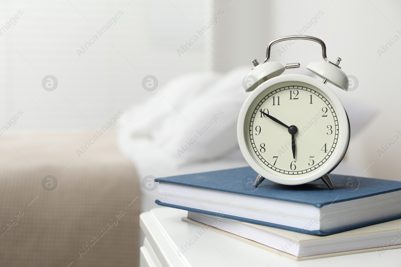 Photo of Alarm clock and books on white nightstand in bedroom, space for text